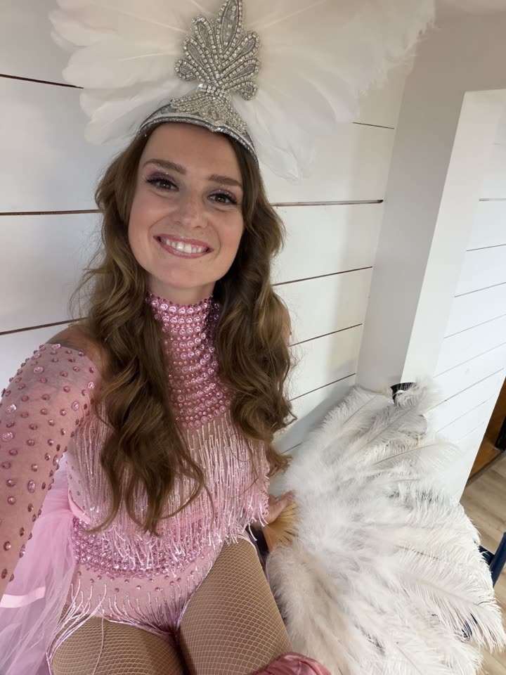 Sarah Grace in a pink rhinestone bodysuit and white feather headdress, backstage portrait