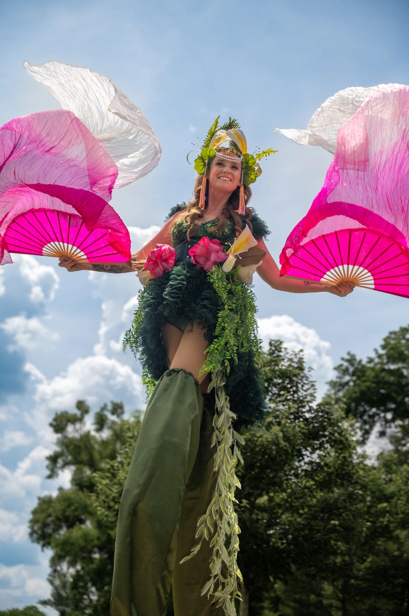 Sarah Grace performing on stilts with pink and white fans in a custom botanical costume